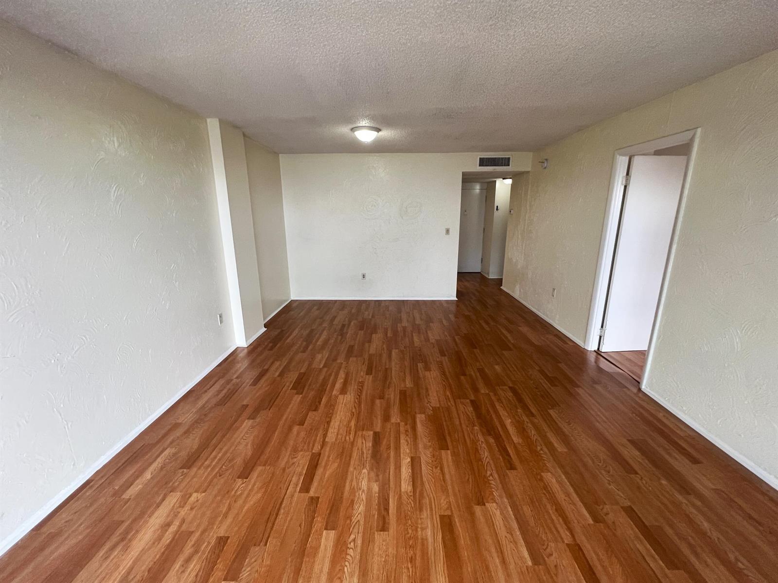 An empty room with light-colored textured walls and wood-look laminate flooring — 15600 NW 7th Avenue # 516, Miami FL 33169, MIAMI, FL