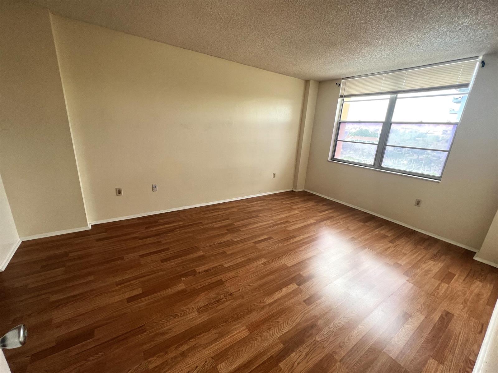 An empty room with wood-look flooring, beige walls, and a window with blinds — 15600 NW 7th Avenue # 516, Miami FL 33169, MIAMI, FL