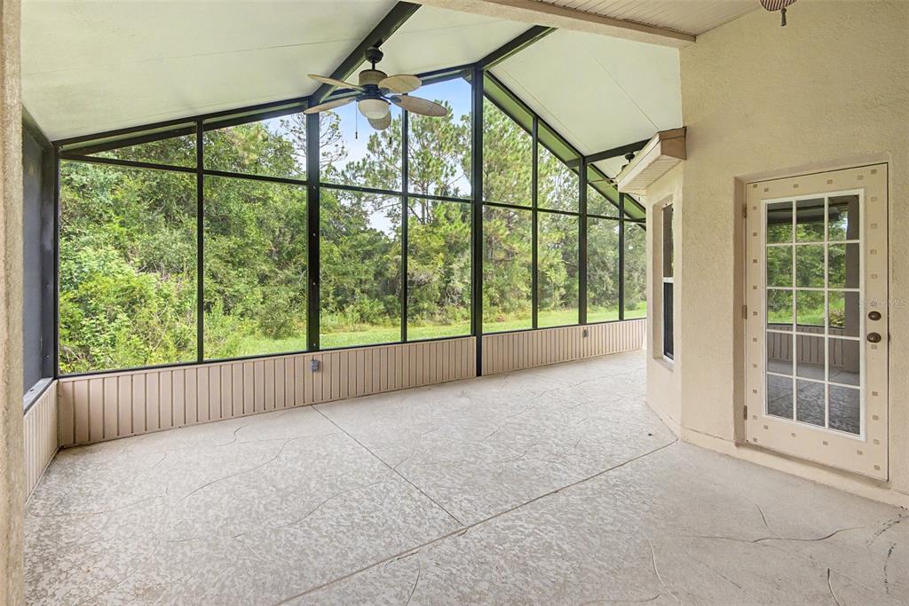 A screened-in porch with a vaulted ceiling, ceiling fan, concrete floor, and view of trees — 204 GRAND CANAL DRIVE, KISSIMMEE, FL