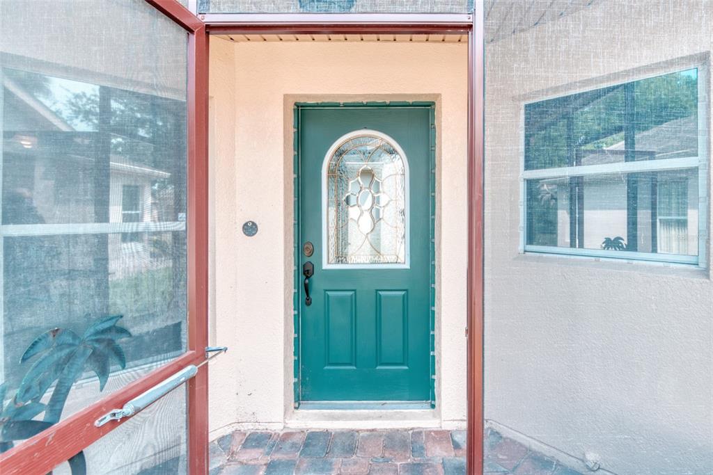 A teal front door with a decorative glass insert sits within a screened-in entryway — 204 GRAND CANAL DRIVE, KISSIMMEE, FL