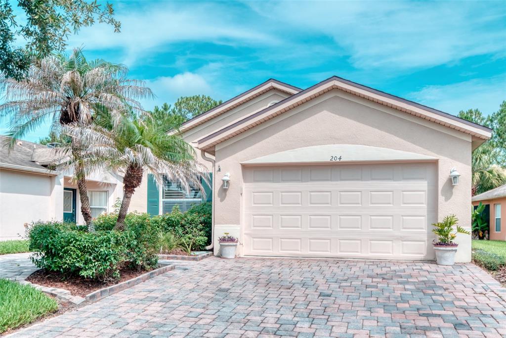 A beige house with a two-car garage and a paved driveway under a blue sky — 204 GRAND CANAL DRIVE, KISSIMMEE, FL