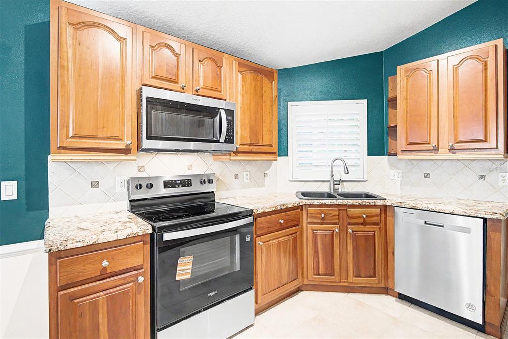 A kitchen features wood cabinets, granite countertops, stainless steel appliances, and dark teal walls — 204 GRAND CANAL DRIVE, KISSIMMEE, FL