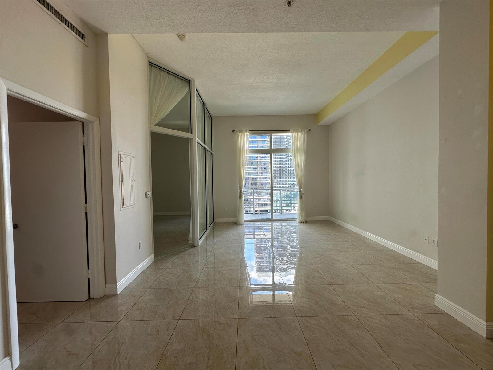 An empty room with beige tile flooring, white walls, and a balcony with city views — 234 NE 3rd Street, Miami FL 33132, MIAMI, FL