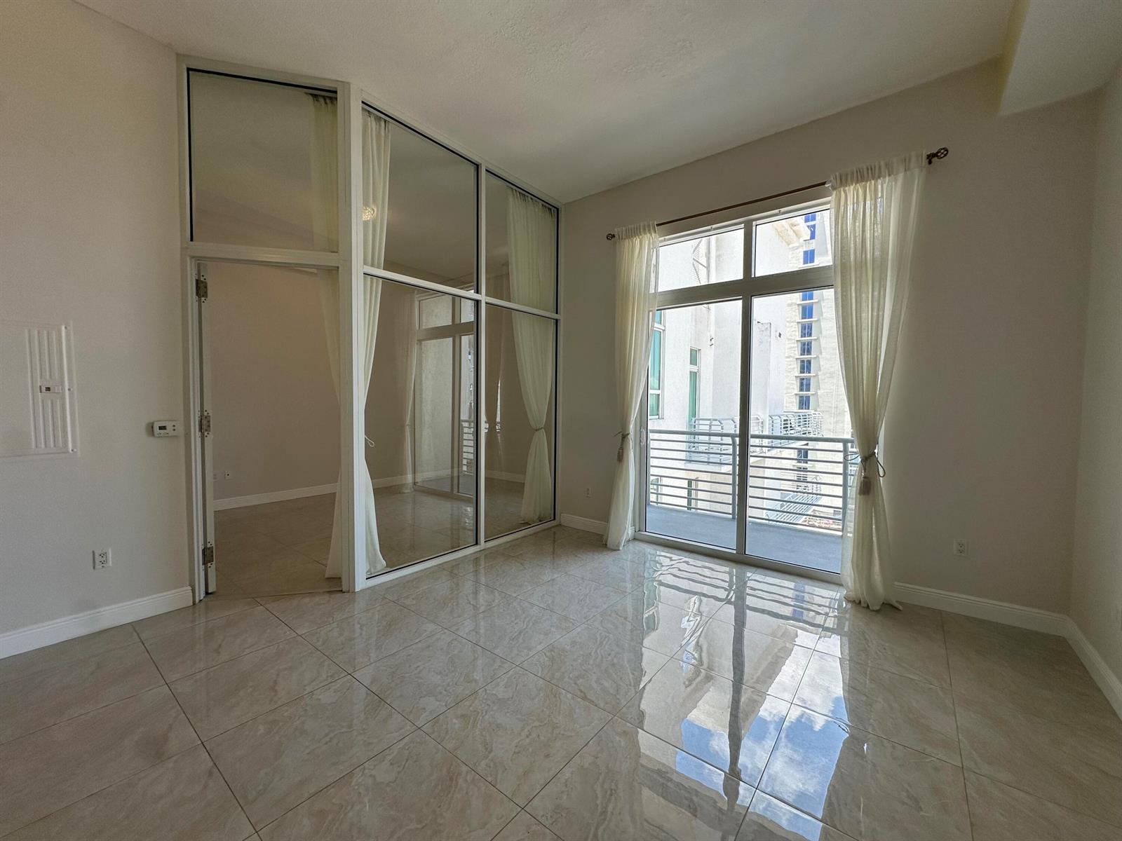 A room with light-colored tile flooring, a glass-enclosed office space, and a balcony door — 234 NE 3rd Street, Miami FL 33132, MIAMI, FL