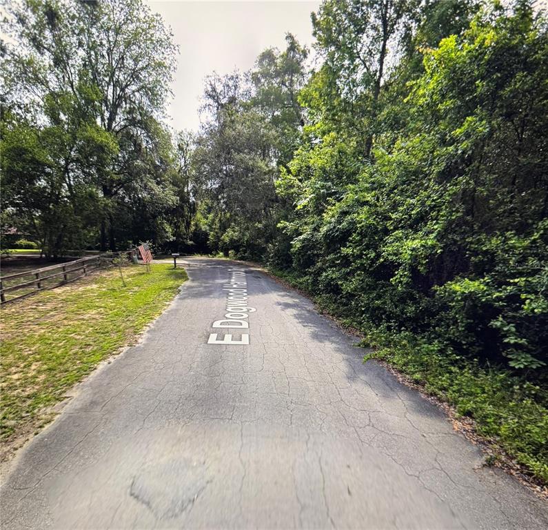 A paved road winds through a wooded area with a wooden fence on the left — 6761 E DOGWOOD HAMMOCK DRIVE, INVERNESS, FL
