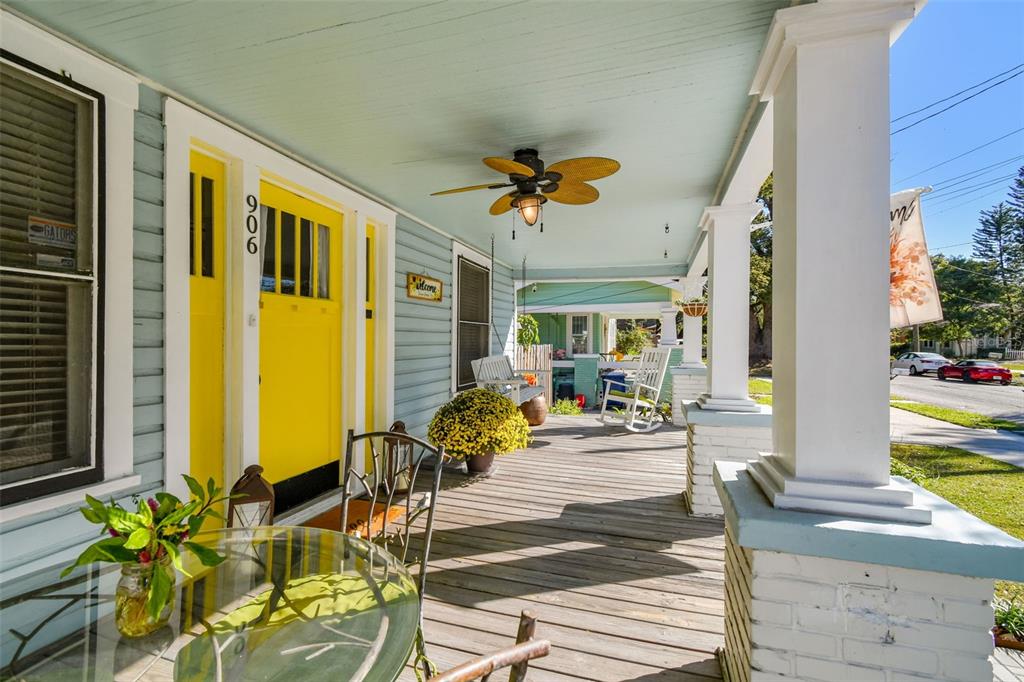 A covered wooden front porch features a bright yellow door, a ceiling fan, and seating — 906 E HAMILTON AVENUE, TAMPA, FL