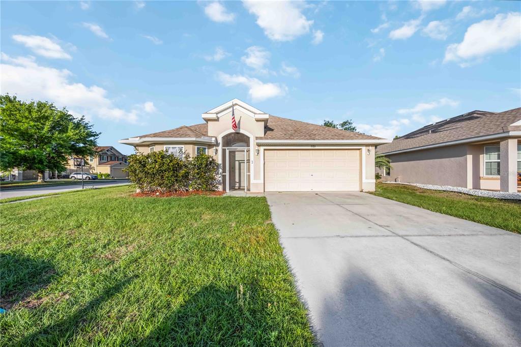 A single-story suburban house with a beige exterior, a two-car garage, and a concrete driveway — 9984 SPRING GULCH LANE, PUNTA GORDA, FL