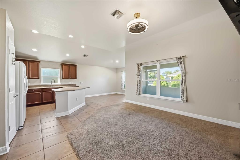 A kitchen with brown cabinets and tile flooring opens into a carpeted dining area — 9984 SPRING GULCH LANE, PUNTA GORDA, FL