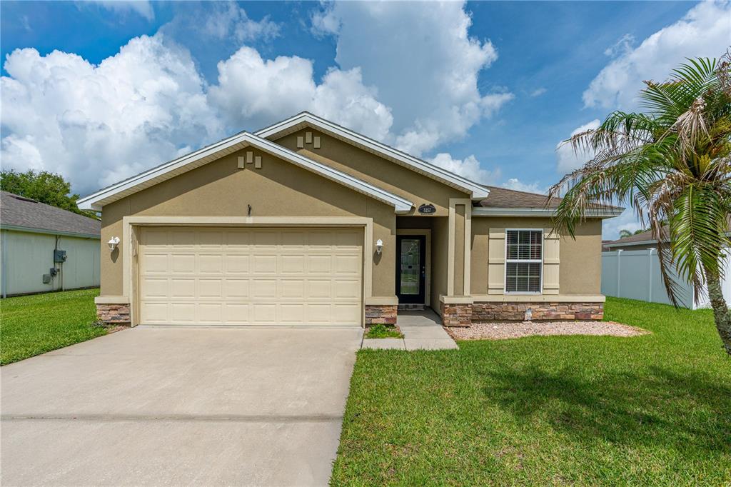 A single-story house with a tan stucco exterior, stone accents, and a two-car garage — 5257 PLANTATION HOME WAY, PORT ORANGE, FL