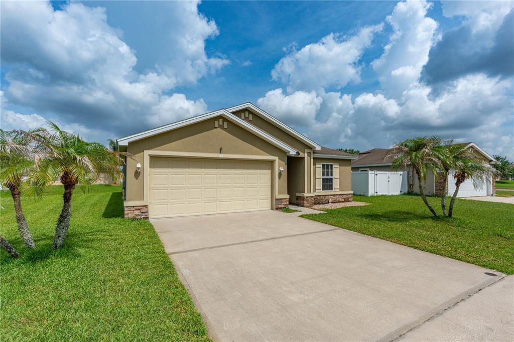 A single-story house with a beige stucco exterior, stone accents, and a two-car garage — 5257 PLANTATION HOME WAY, PORT ORANGE, FL