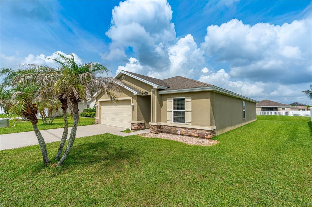 A single-story tan house with a two-car garage, stone accents, and a palm tree — 5257 PLANTATION HOME WAY, PORT ORANGE, FL