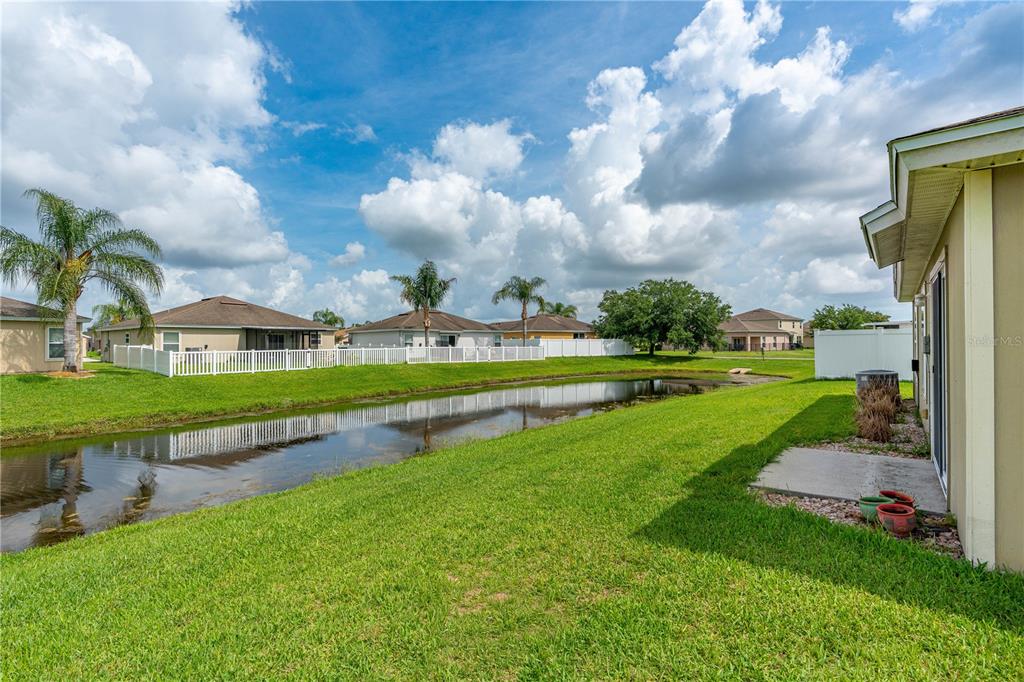 A view of a backyard with a small pond, green lawn, and neighboring houses — 5257 PLANTATION HOME WAY, PORT ORANGE, FL