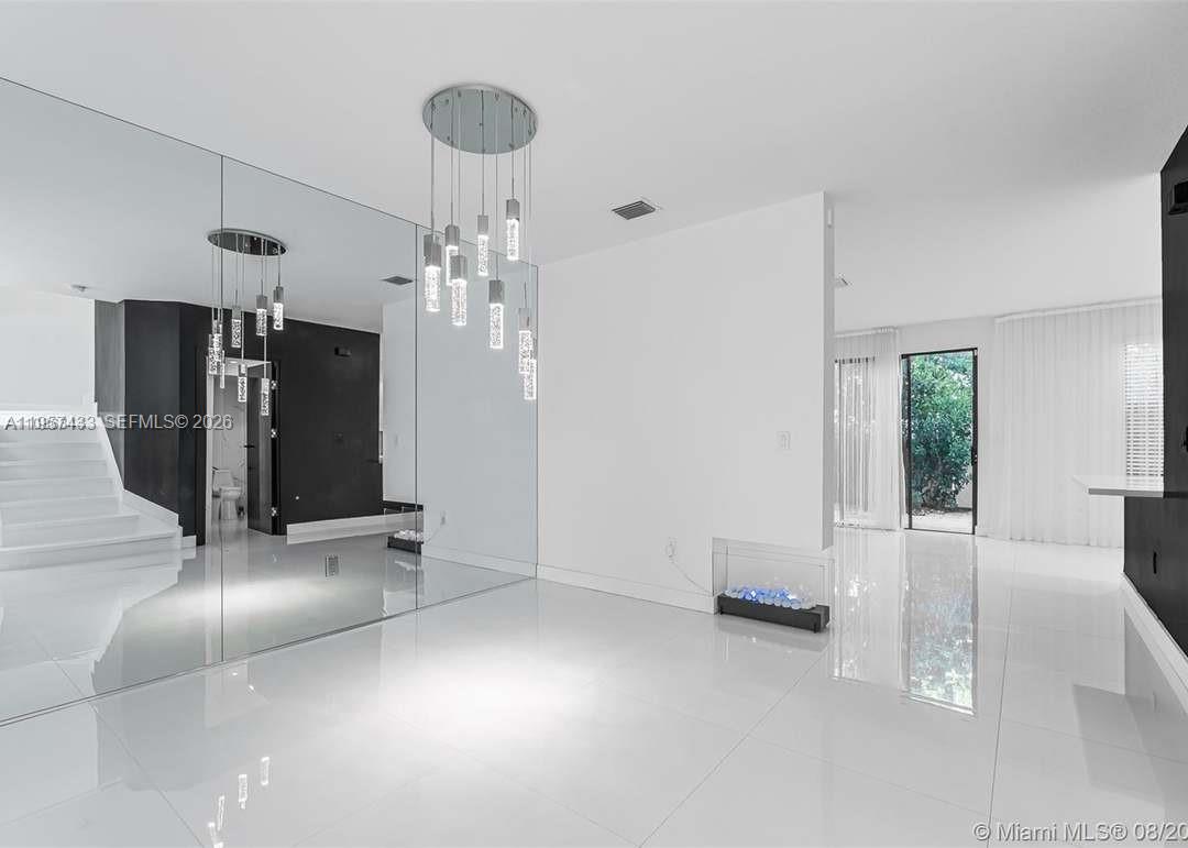 A modern, minimalist room features white tile floors, a mirrored wall, and a pendant chandelier — 10301 W 32nd Ln, Hialeah FL 33018, HIALEAH, FL