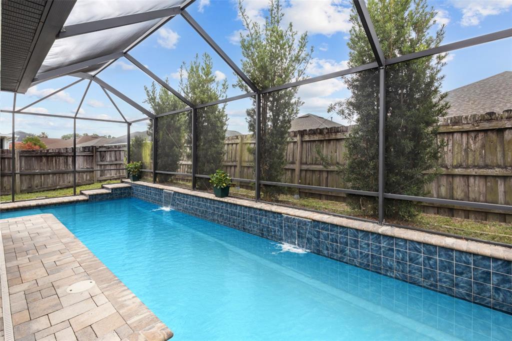 A screened-in swimming pool with two water features and a paver deck in a backyard — 22633 MARSH WREN DRIVE, LAND O LAKES, FL