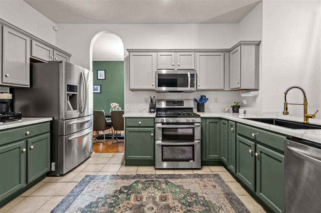 A kitchen features two-toned gray and green cabinets, stainless steel appliances, and a patterned rug — 22633 MARSH WREN DRIVE, LAND O LAKES, FL