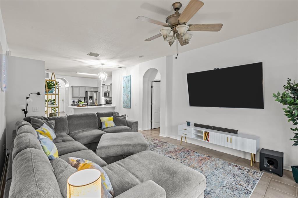 A living room features a gray sectional sofa, a wall-mounted television, and an open kitchen — 22633 MARSH WREN DRIVE, LAND O LAKES, FL