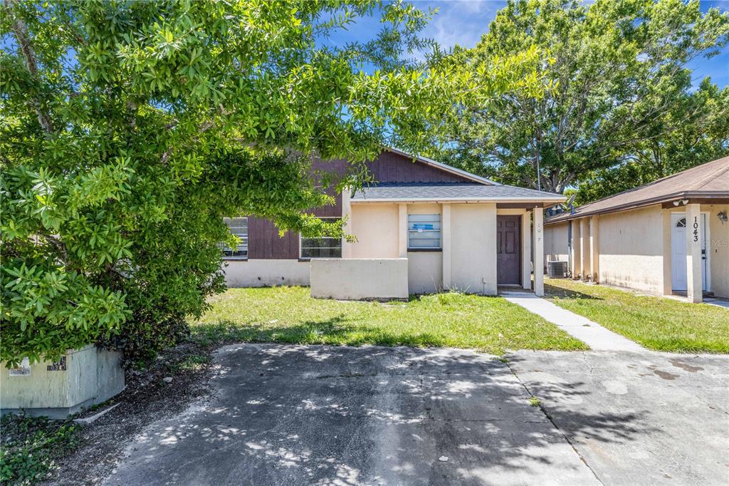 A single-story duplex with a concrete driveway, a small front yard, and a large tree — 1047 / 1049 CAPTIVA POINT, LAKELAND, FL