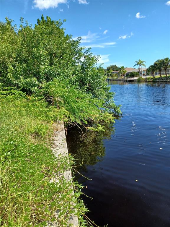 A concrete seawall borders a grassy bank next to a canal with trees and houses — 4195 SPIRE STREET, PORT CHARLOTTE, FL
