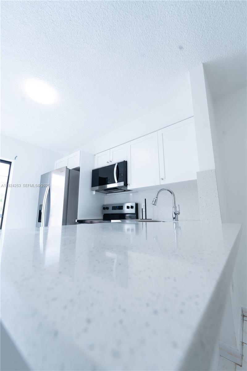 A modern kitchen features white cabinets, stainless steel appliances, and a white speckled countertop — 5300 W 21st Ct # 311, Hialeah FL 33016, HIALEAH, FL