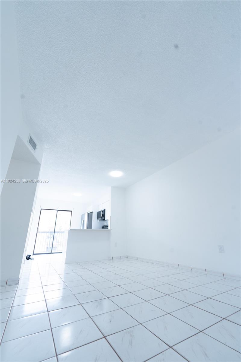 An empty room with white tile floors leads to a kitchen with a breakfast bar — 5300 W 21st Ct # 311, Hialeah FL 33016, HIALEAH, FL
