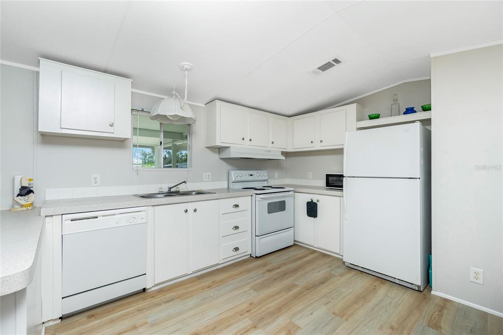 A kitchen features white cabinetry, white appliances, light countertops, and wood-look flooring — 7364 TISA AVENUE, PORT CHARLOTTE, FL
