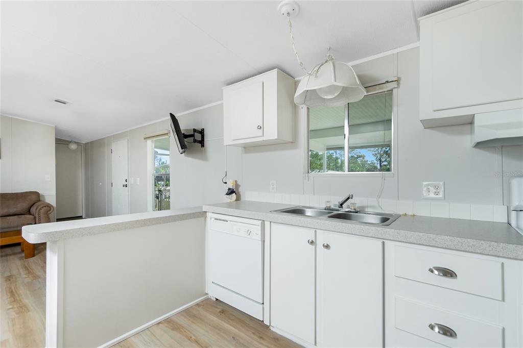 A kitchen with white cabinets, a double sink, and a dishwasher overlooks a living area — 7364 TISA AVENUE, PORT CHARLOTTE, FL