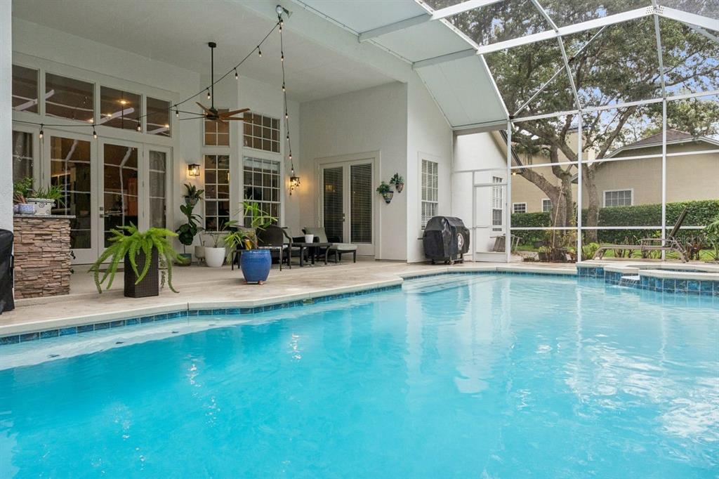 A screened-in patio features a swimming pool, stone-accented outdoor kitchen, and string lighting — 1647 EAGLE NEST CIRCLE, WINTER SPRINGS, FL