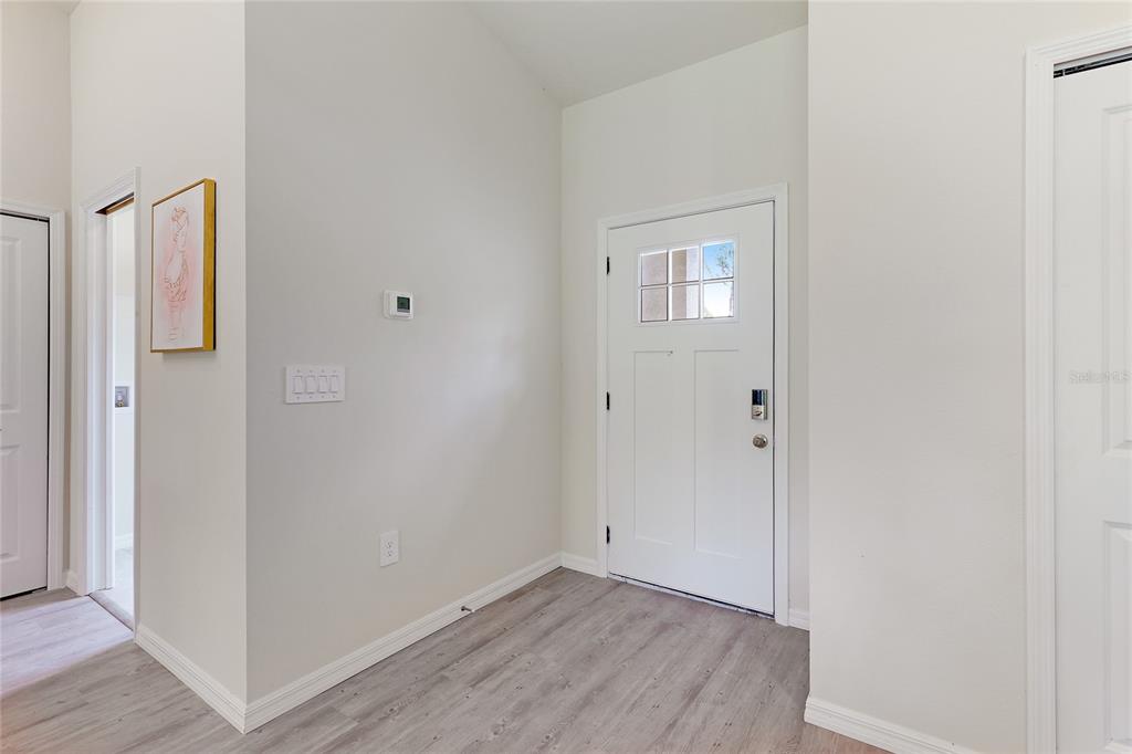 An entryway features light wood-look flooring, white walls, a white front door, and a thermostat — 3837 URIAH STREET, NORTH PORT, FL