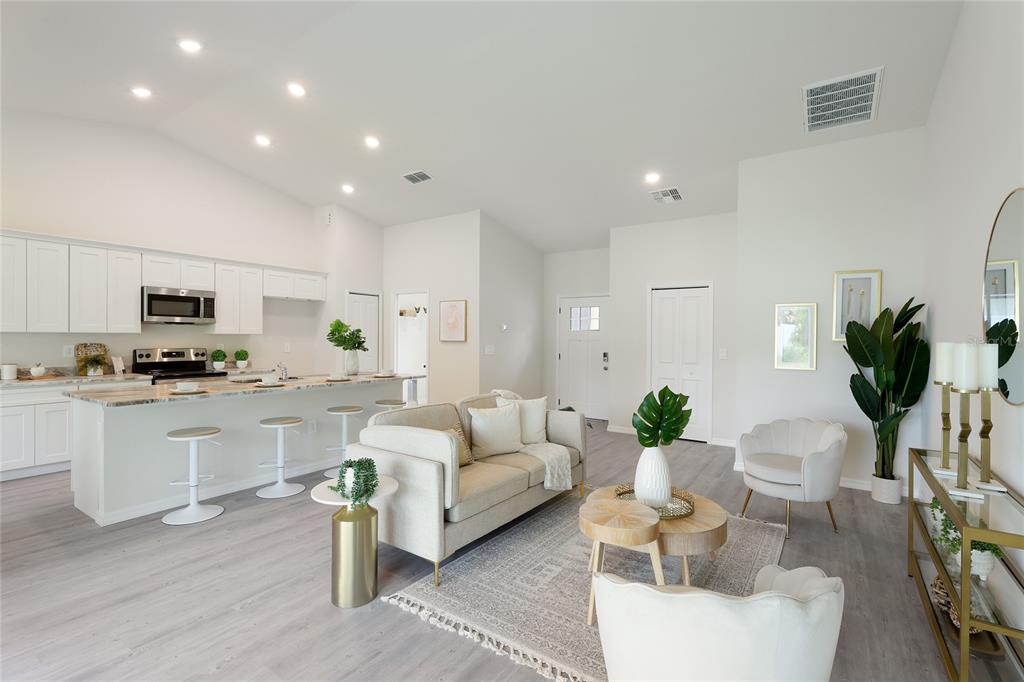 An open-concept living room and kitchen featuring white cabinetry, light wood flooring, and neutral furniture — 3837 URIAH STREET, NORTH PORT, FL