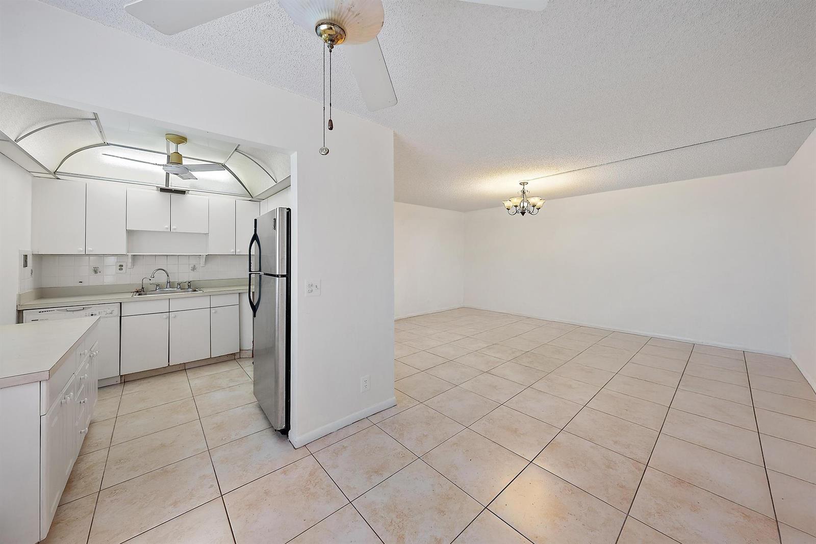 A kitchen with white cabinets and stainless steel appliances opens to a tiled dining area — 869 S Flanders S, Delray Beach FL 33484, DELRAY BEACH, FL