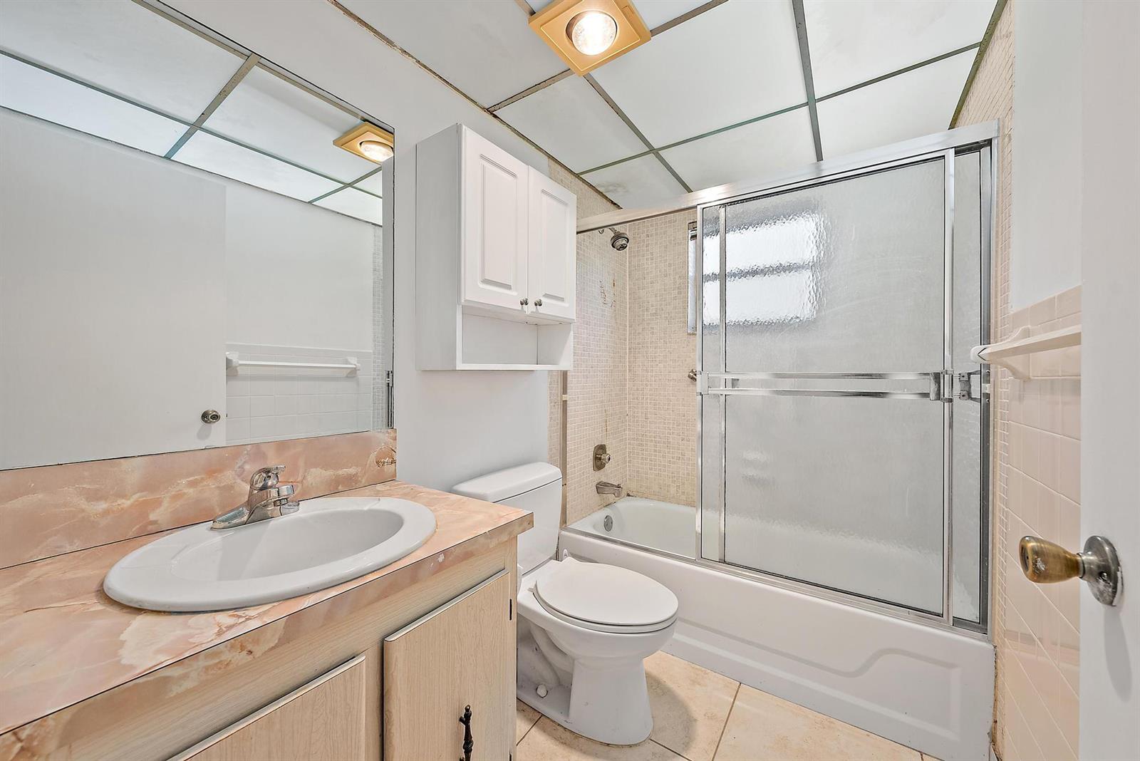A bathroom features a vanity with a pink countertop, a toilet, and a shower-tub combo — 869 S Flanders S, Delray Beach FL 33484, DELRAY BEACH, FL