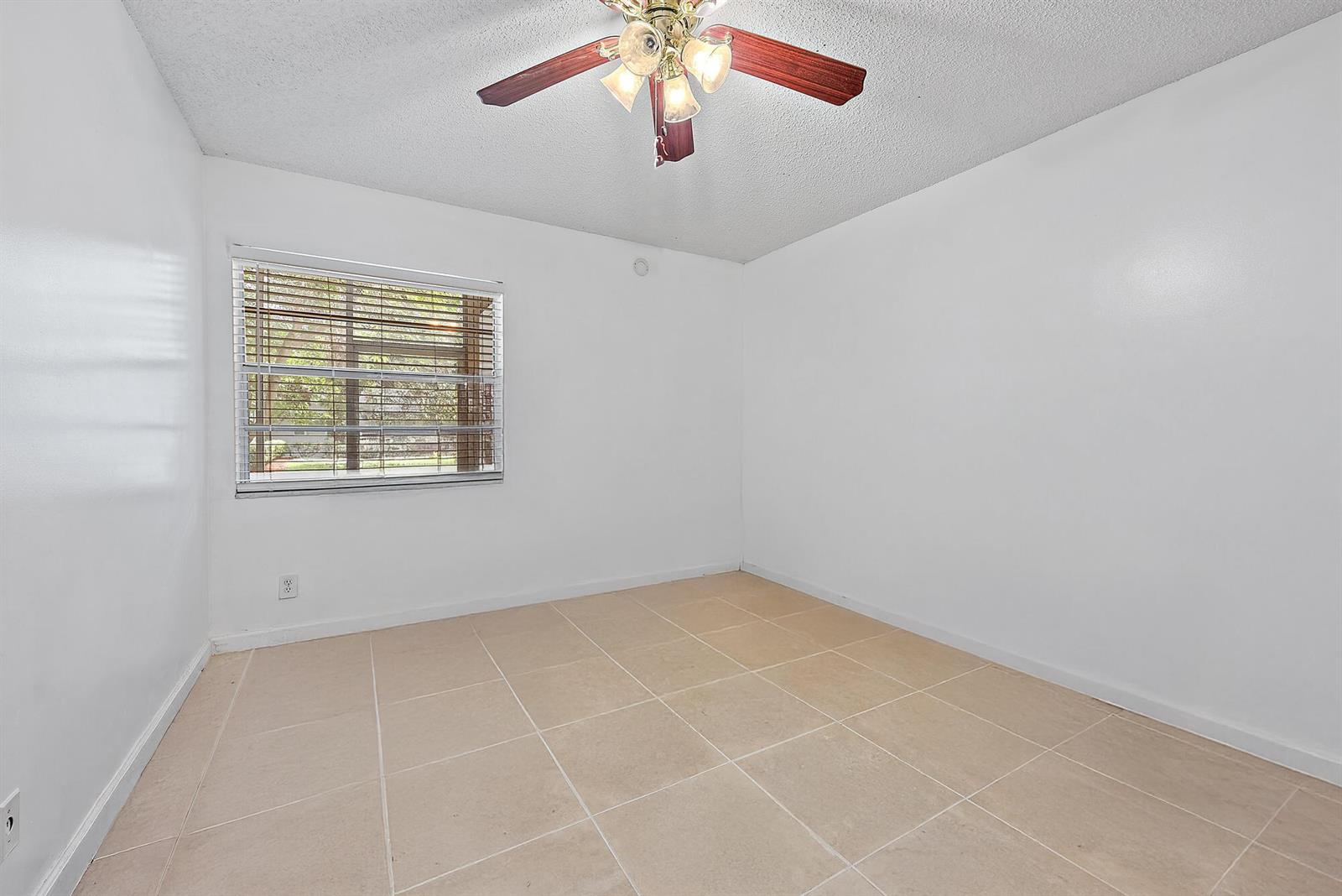 An empty bedroom features white walls, beige tile flooring, and a ceiling fan — 869 S Flanders S, Delray Beach FL 33484, DELRAY BEACH, FL