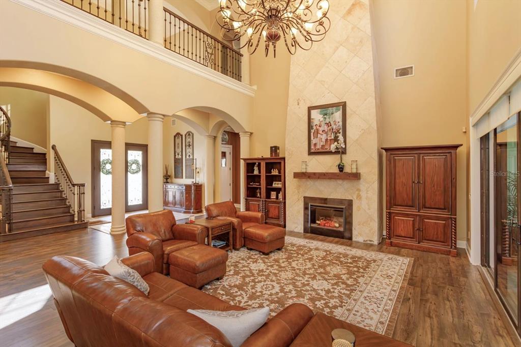A two-story living room features a stone fireplace, leather furniture, and a large chandelier — 5719 EMERSON POINTE WAY, ORLANDO, FL