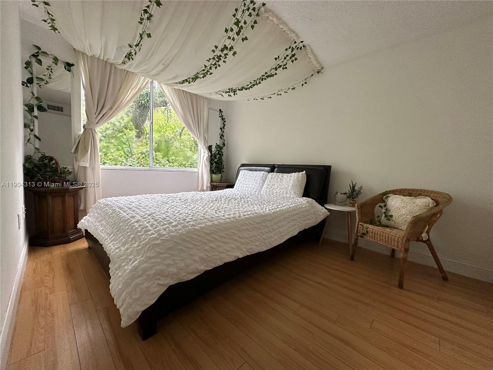A bedroom features a bed with white textured bedding, draped ceiling fabric, and a wicker chair — 1720 NW N River Dr # 305, Miami FL 33125, MIAMI, FL