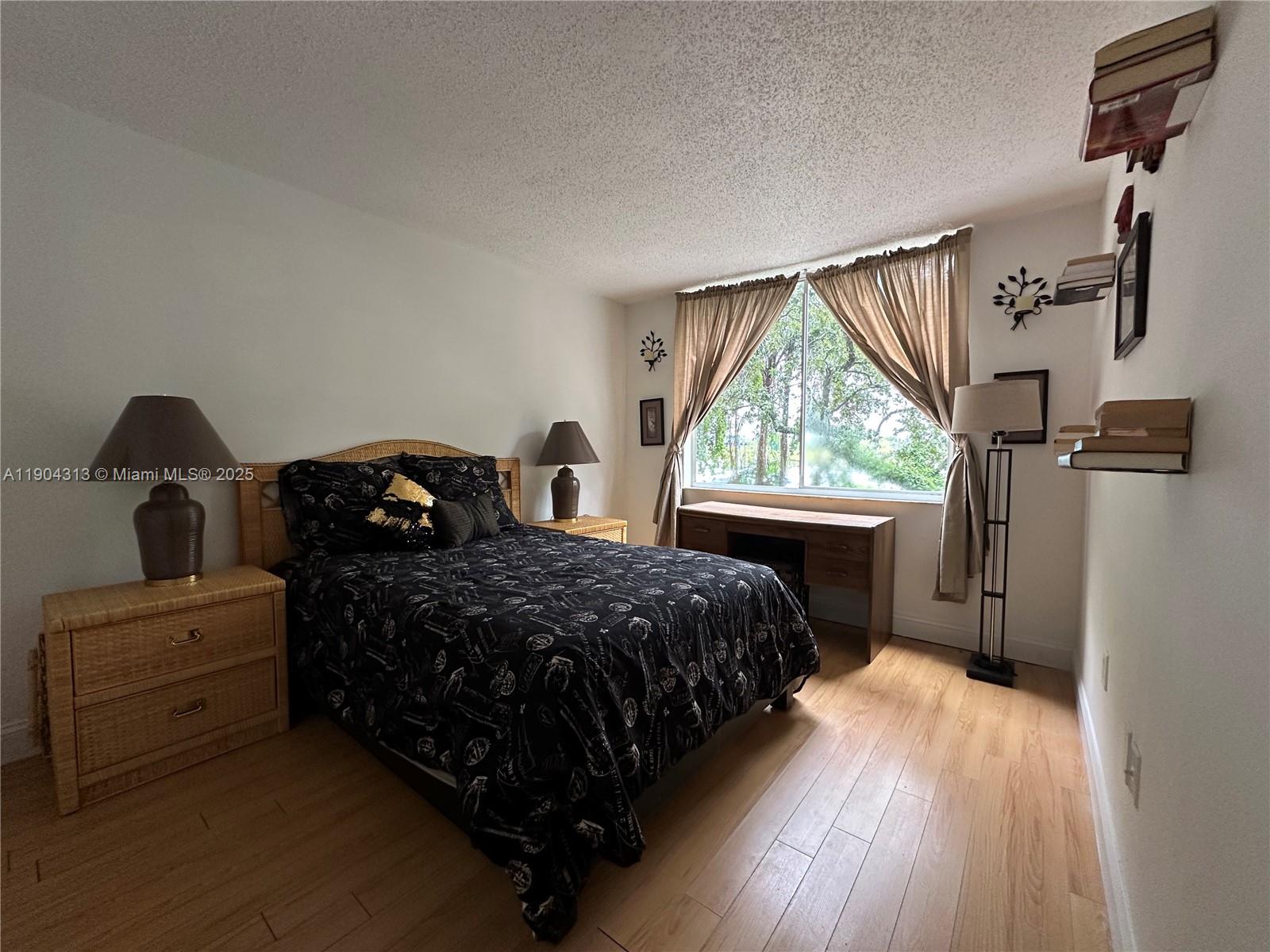A bedroom features a bed with black patterned bedding, wicker nightstands, and a wooden desk — 1720 NW N River Dr # 305, Miami FL 33125, MIAMI, FL