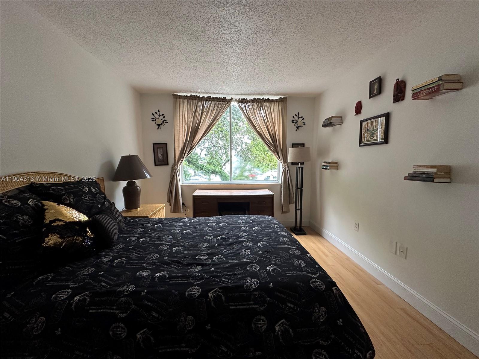 A bedroom features a bed with black patterned bedding, a window, and wall-mounted shelves — 1720 NW N River Dr # 305, Miami FL 33125, MIAMI, FL