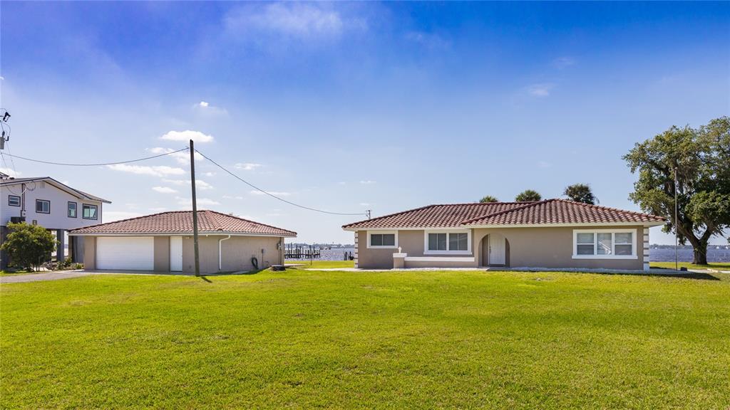 A tan house and a detached garage sit on a large lawn near the water — 1808 STEVENSON ROAD, NORTH FORT MYERS, FL