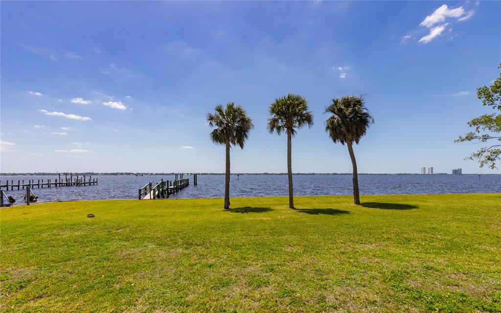 A grassy lawn leads to a waterfront view with three palm trees and a wooden dock — 1808 STEVENSON ROAD, NORTH FORT MYERS, FL