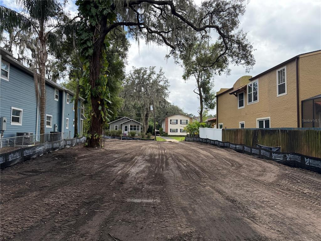 A vacant, dirt-covered residential lot sits between two multi-story buildings under a large tree — 1105 ELMWOOD STREET, ORLANDO, FL