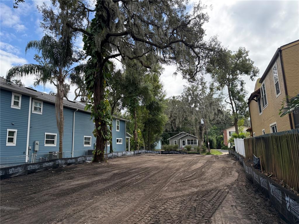 A vacant, cleared dirt lot sits between two multi-story residential buildings under large trees — 1105 ELMWOOD STREET, ORLANDO, FL