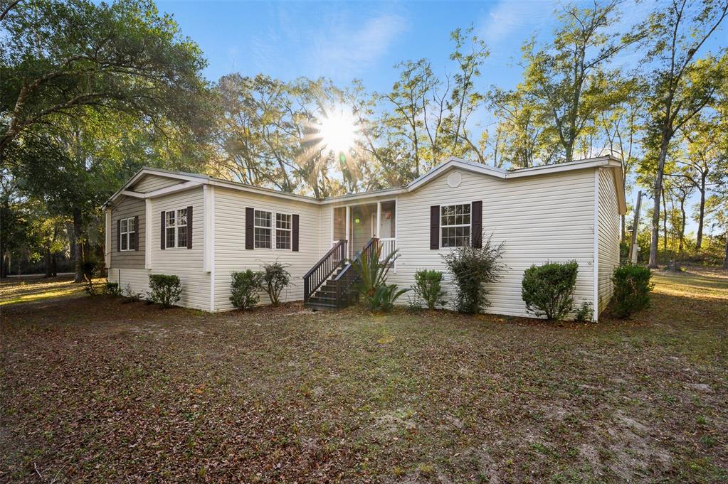 A single-story house with light siding and a front porch sits on a wooded lot — 13076 SW 154TH STREET, ARCHER, FL