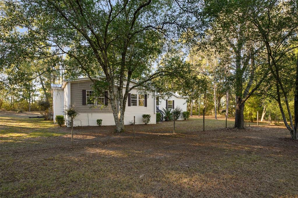 A light-colored manufactured home with a recessed entrance and dark shutters sits on a lot — 13076 SW 154TH STREET, ARCHER, FL