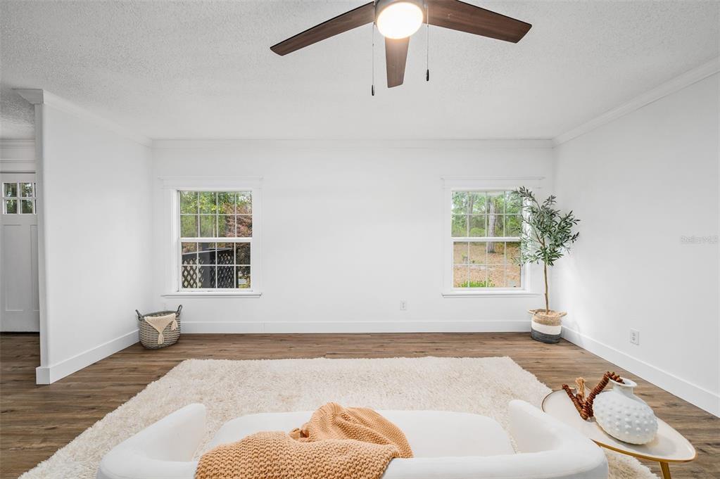 A bright living room features white walls, wood-look flooring, two windows, and a ceiling fan — 13076 SW 154TH STREET, ARCHER, FL