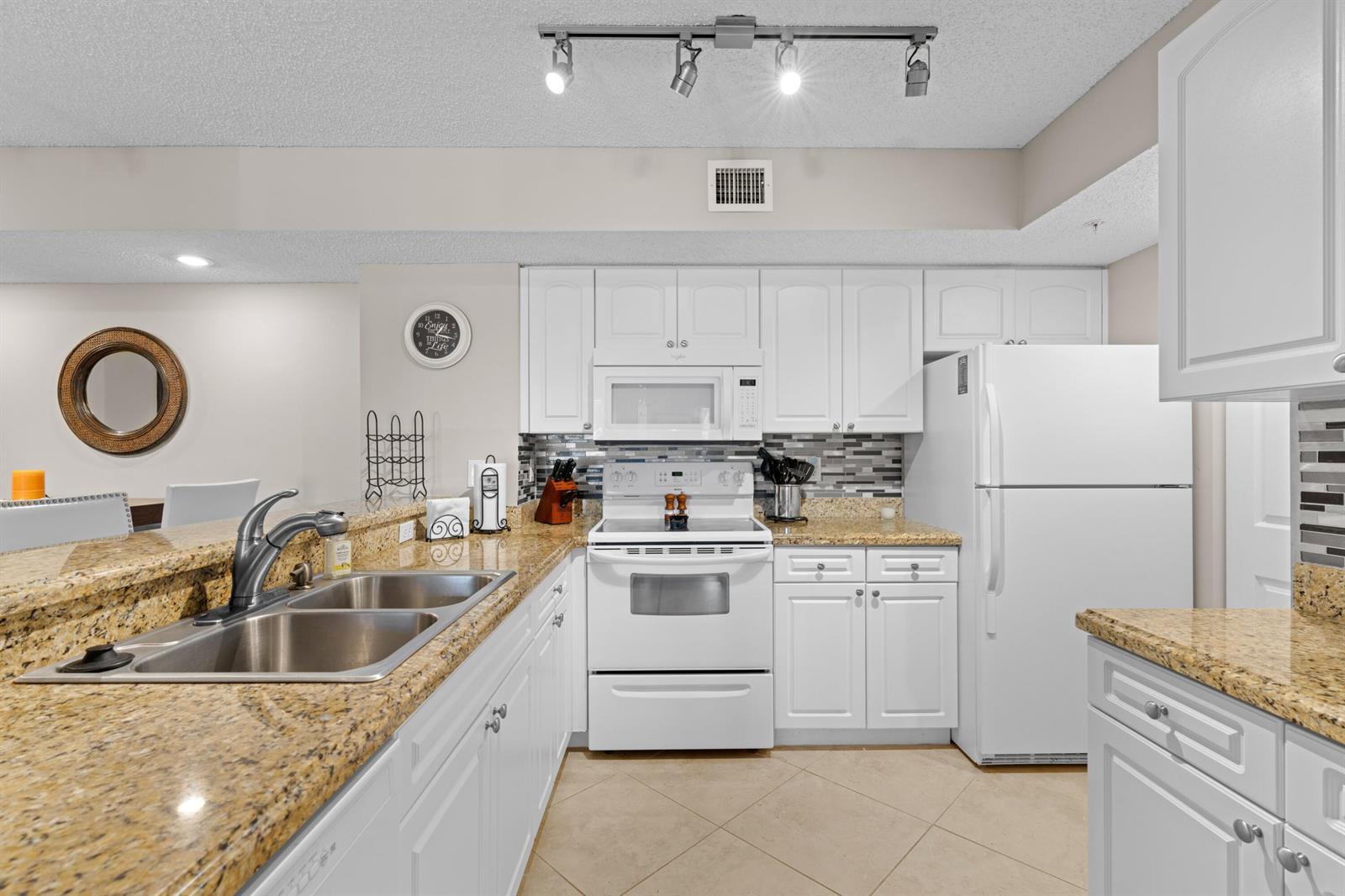 A kitchen features white cabinets, granite countertops, a white stove, and a white refrigerator — 272 Village Boulevard # 7109, Tequesta FL 33469, TEQUESTA, FL