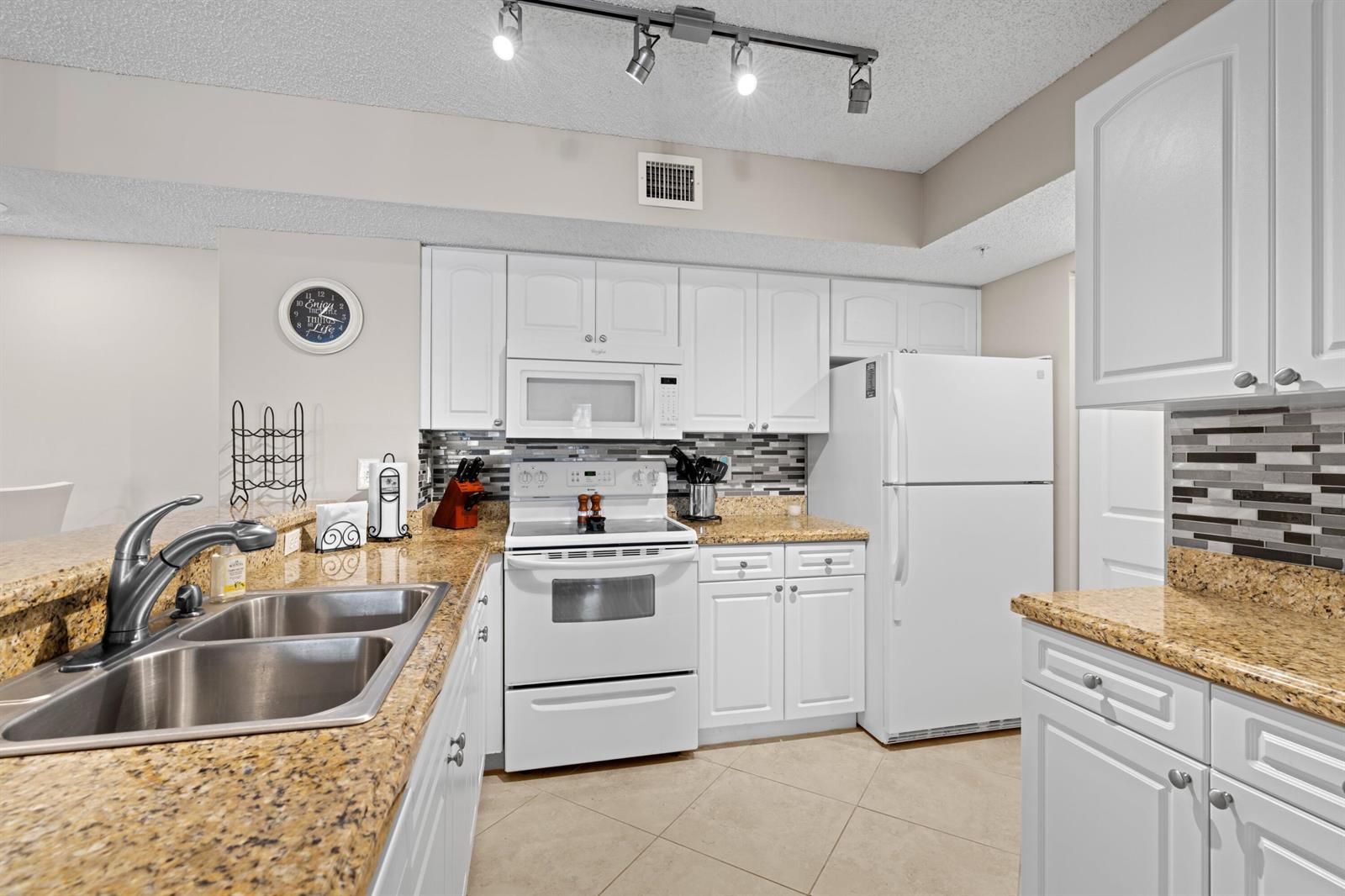 A kitchen features white cabinets, granite countertops, a double sink, and white appliances — 272 Village Boulevard # 7109, Tequesta FL 33469, TEQUESTA, FL