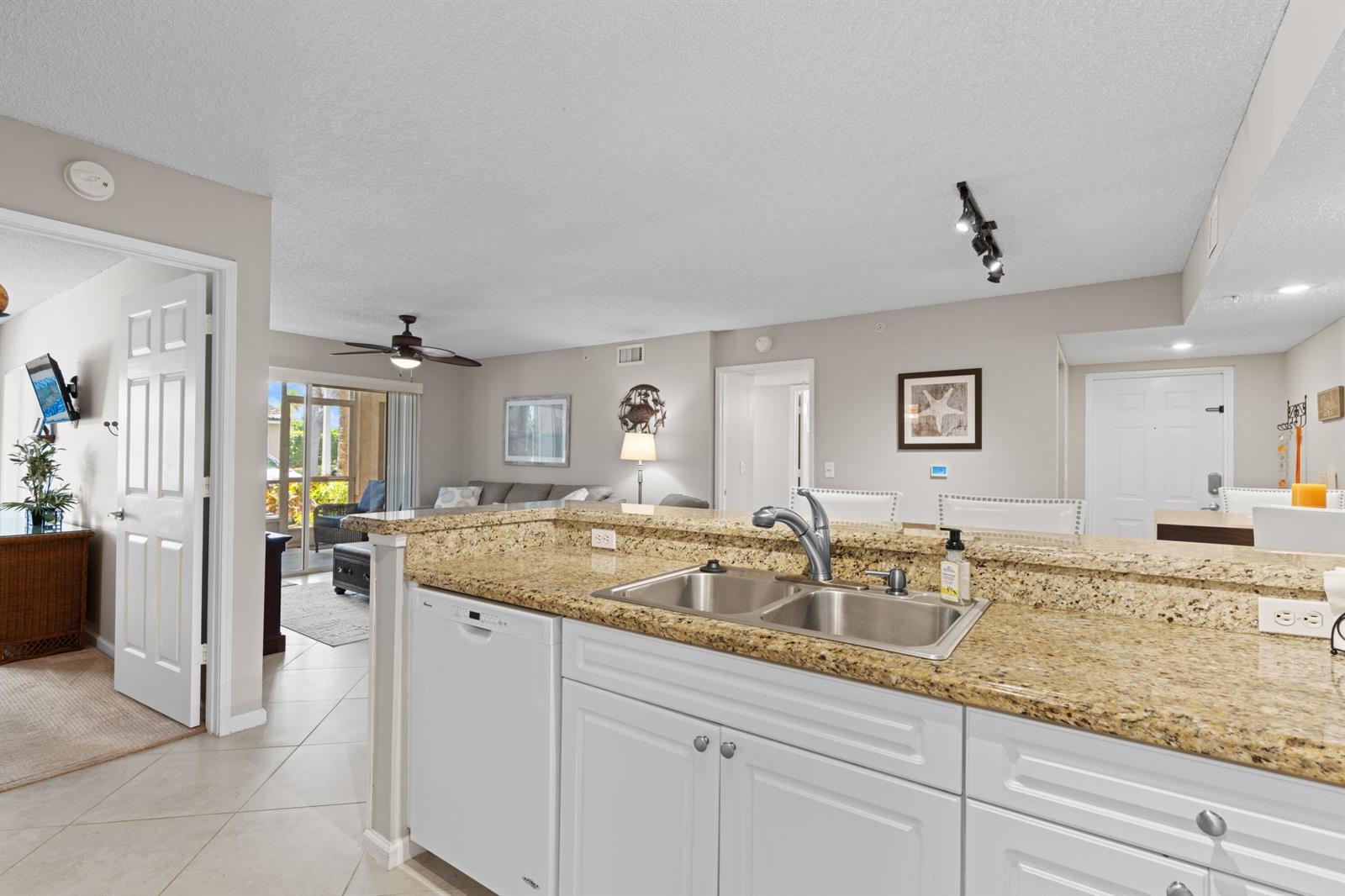 A kitchen with granite countertops and white cabinets overlooks a living area and patio — 272 Village Boulevard # 7109, Tequesta FL 33469, TEQUESTA, FL