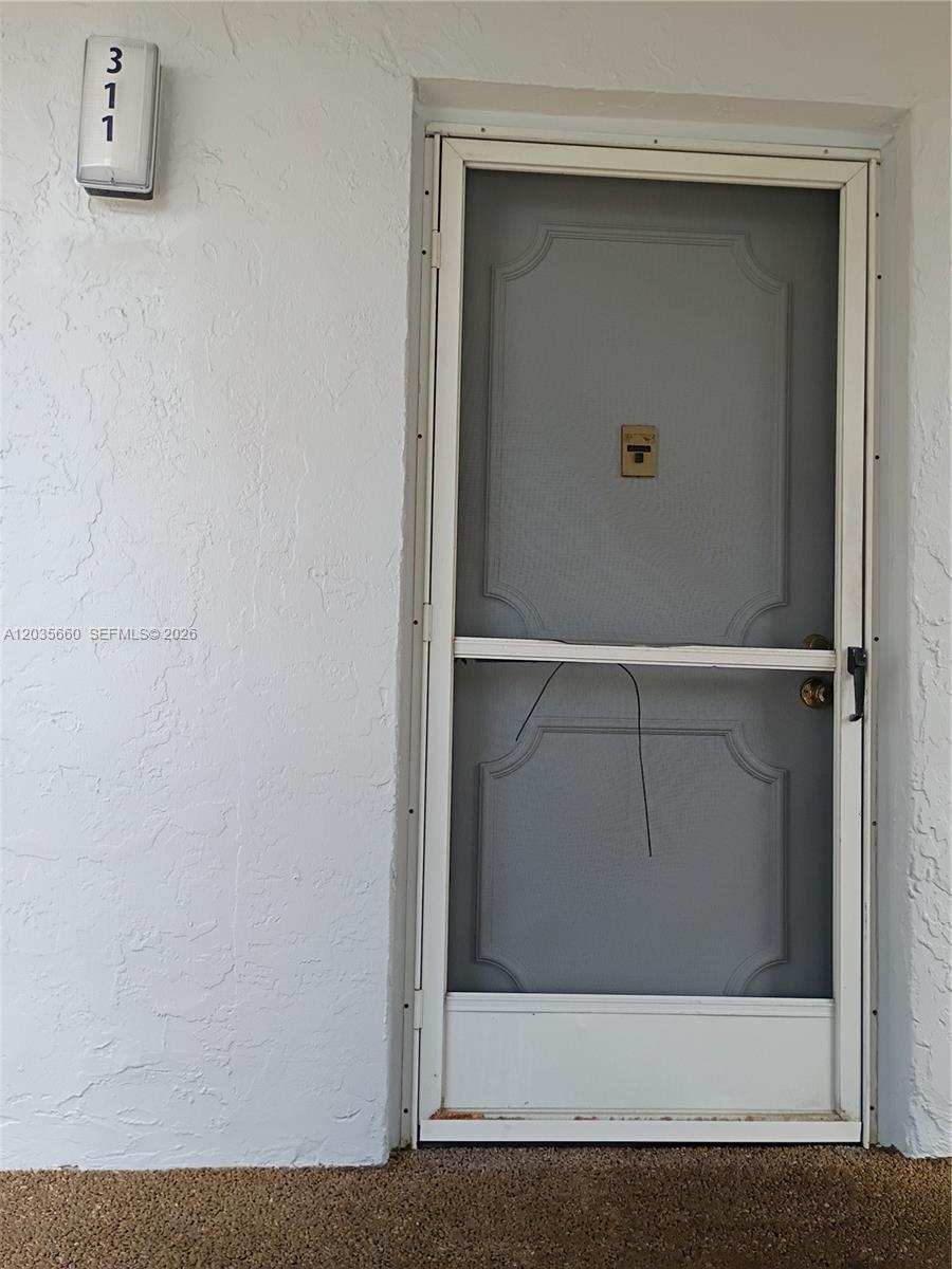 A white exterior wall features a unit number sign and a grey screen door — 3040 Holiday Springs Blvd # 311, Margate FL 33063, MARGATE, FL