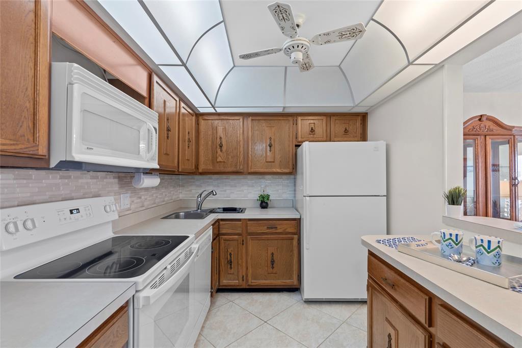 A kitchen features wood cabinets, white appliances, a tiled backsplash, and a vaulted ceiling — 4900 BRITTANY DRIVE S UNIT 808, ST PETERSBURG, FL