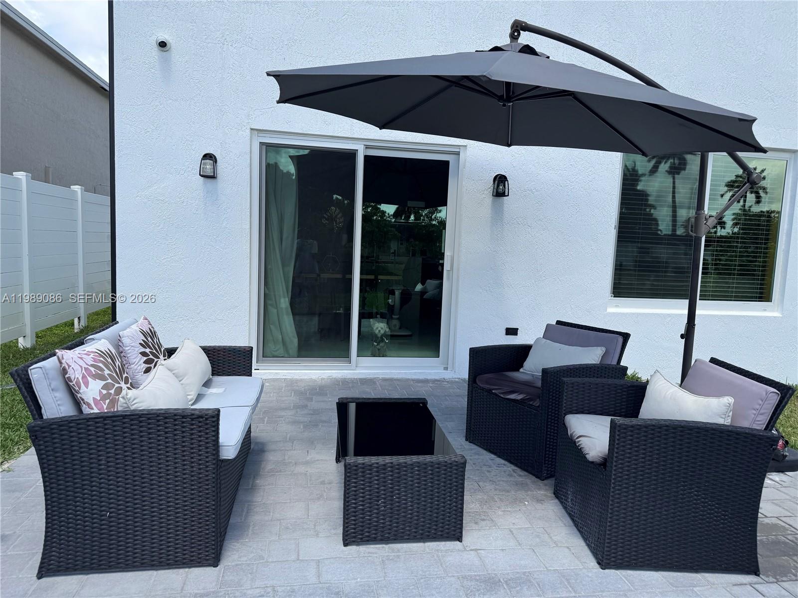 A patio features a black wicker furniture set, a cantilever umbrella, and a sliding glass door — 1236 NW 208th St, Miami Gardens FL 33169, MIAMI GARDENS, FL