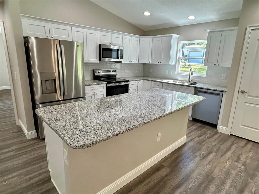 A kitchen features white cabinets, granite countertops, stainless steel appliances, and wood-look flooring — 15637 SE 84TH TERRACE, SUMMERFIELD, FL